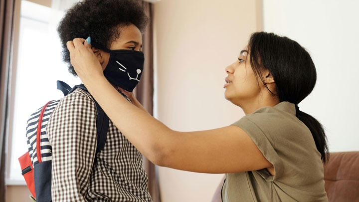 A mother adjusting her son's facemask, illustrating the concept of overprotecting a child.