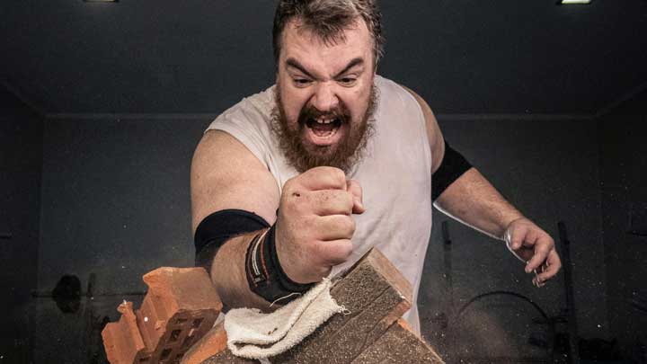 A middle-aged white man breaking bricks with a karate-style punch, showing explosive anger on his face, symbolizing Intermittent Explosive Disorder (IED).