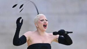 Lady Gaga performing on stage in a black shoulderless dress and black full-sleeve gloves, accented with strange antenna-style wings.