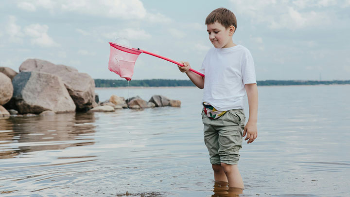 A 10-year-old child standing by the riverside, holding a net and repeatedly trying to catch fish, symbolizing traits of Obsessive-Compulsive Disorder (OCD).