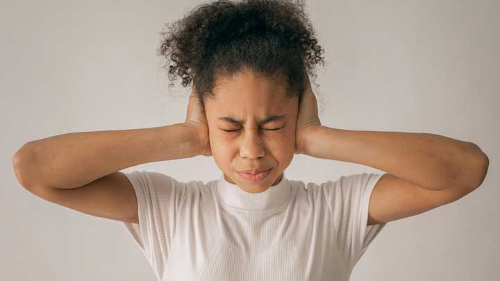 A mixed-race African-American girl closing her eyes and ears forcibly, symbolizing the overwhelming sensory and emotional experiences associated with Social Anxiety Disorder.